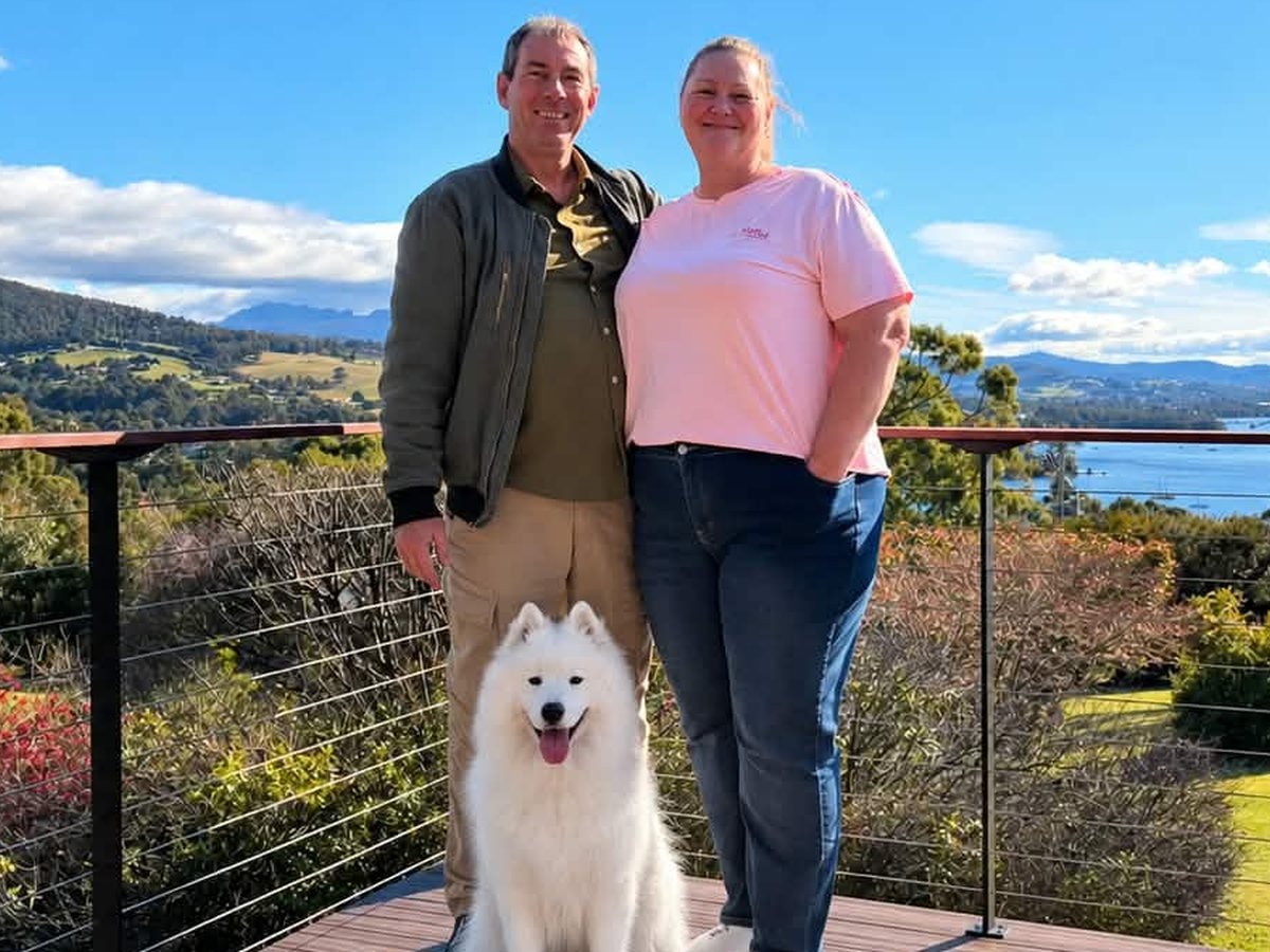 Cherrie, Paul and Holly the Samoyed on a deck overlooking hills and water on Tasmania's North West coast